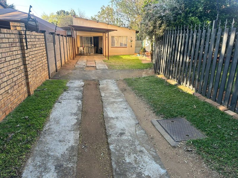 Front exterior view of the property featuring a concrete driveway, brick boundary wall, metal security fencing, and a small covered patio area.