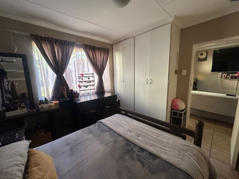 A functional bedroom featuring built-in cupboards, tiled flooring, and a view into the adjacent room.