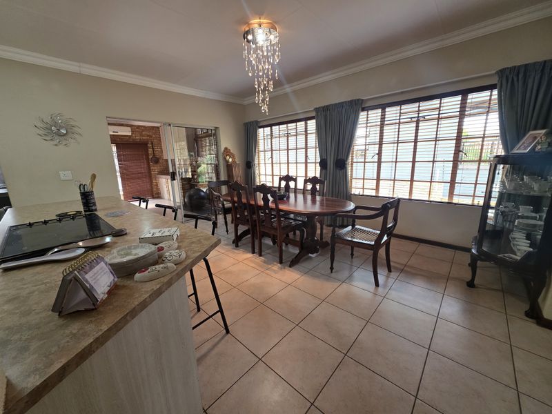 Spacious open-plan dining and kitchen area featuring a central island with a built-in hob, tiled flooring, and large windows providing ample natural light.