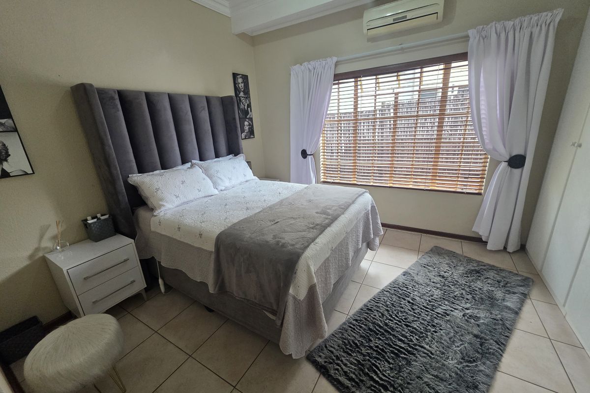 A well-maintained bedroom featuring tiled flooring, built-in cupboards, a wall-mounted air conditioning unit, and wooden venetian blinds.