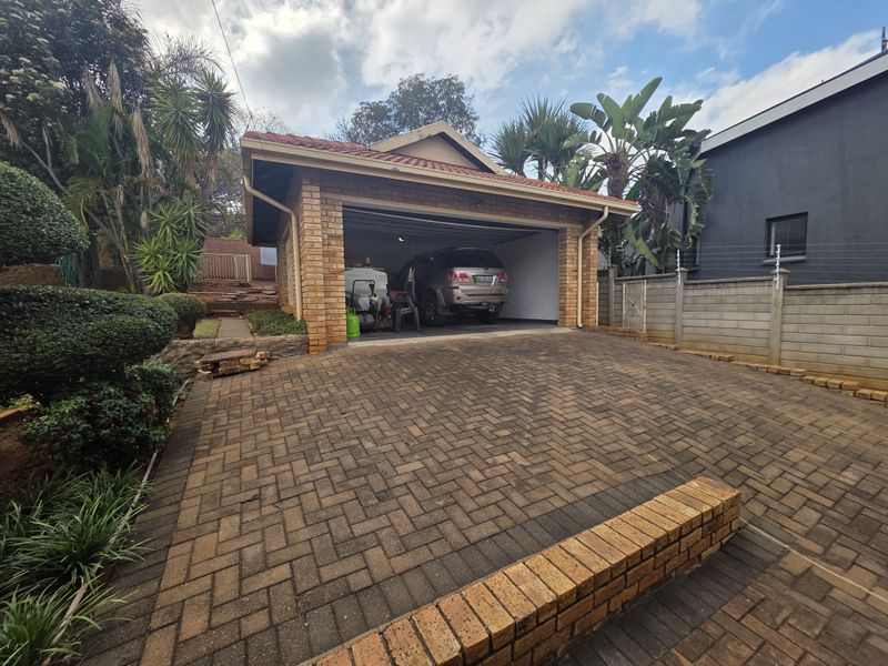 A detached facebrick garage with a tiled roof, featuring a paved driveway and established garden surroundings.