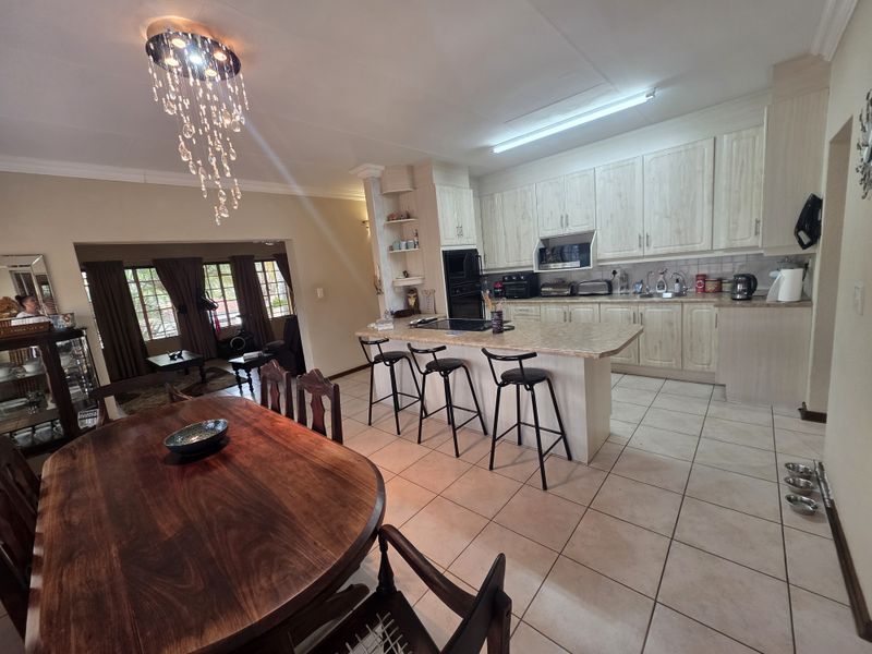 Open-plan kitchen and dining area featuring light-toned cabinetry, a central island with breakfast bar seating, and tiled flooring throughout.