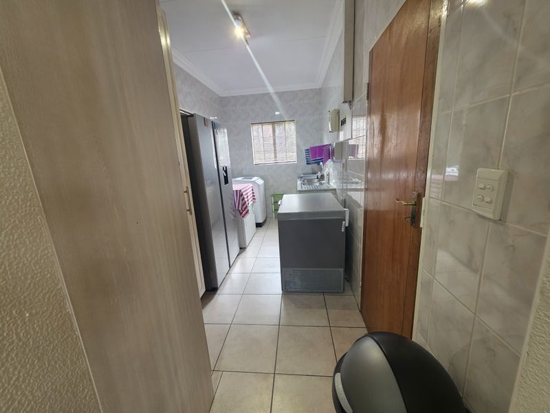 A functional laundry room featuring tiled walls and flooring, equipped with a stainless steel sink and dedicated plumbing connections for appliances.