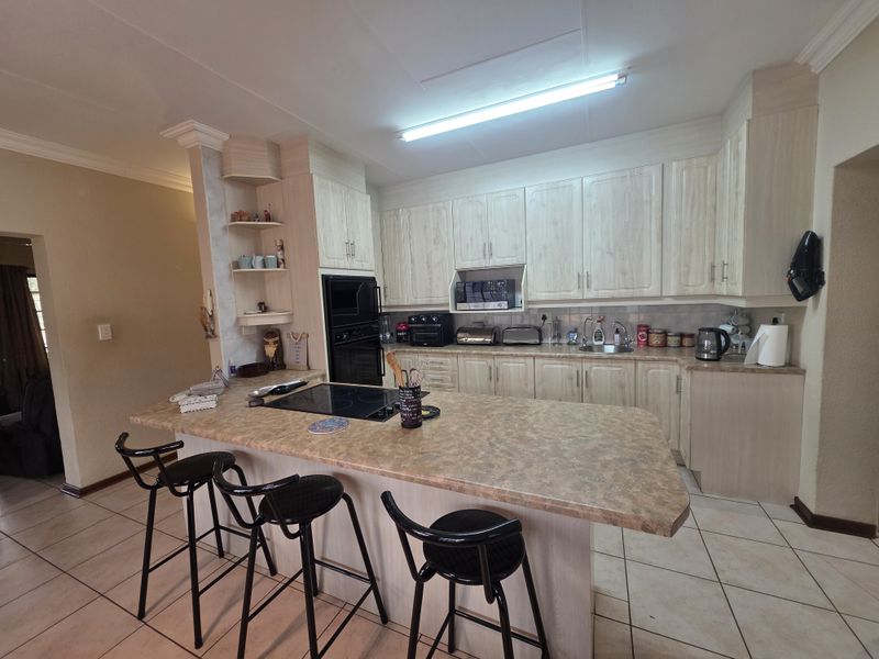 A functional kitchen featuring light-toned cabinetry, laminate countertops, a breakfast bar, and integrated appliances, finished with tiled flooring.