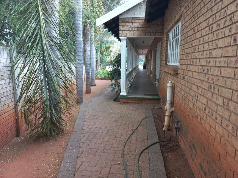 A side view of the property featuring a brick facade, a covered patio walkway, and paved pathways alongside mature trees.