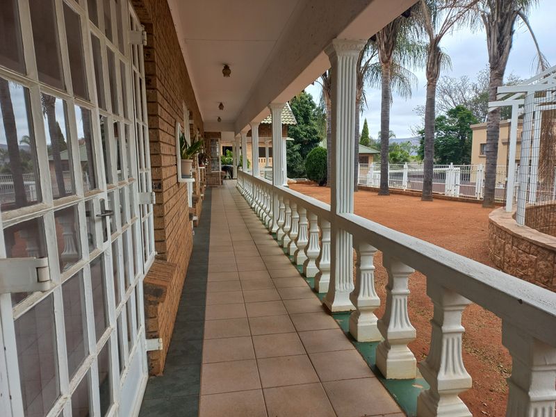 A covered outdoor patio featuring tiled flooring, classic columns, and a decorative balustrade overlooking the garden area.