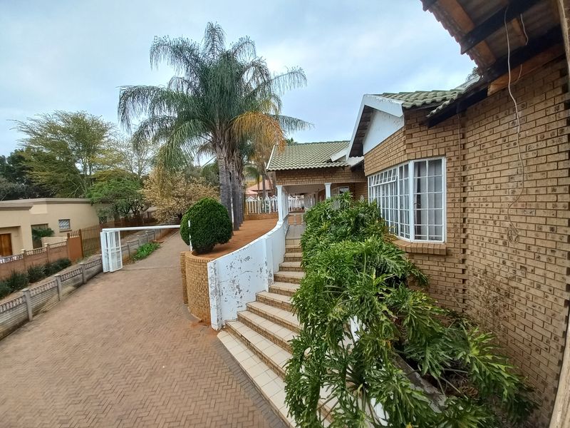 Front exterior view of a brick house featuring a paved driveway, concrete staircase, and established garden landscaping.