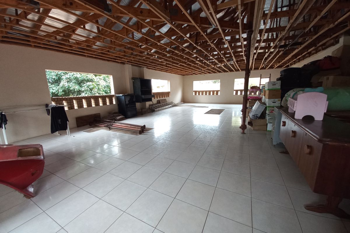 Spacious open-plan living area featuring tiled flooring, a built-in fireplace, and exposed timber roof trusses, offering a blank canvas for renovation.