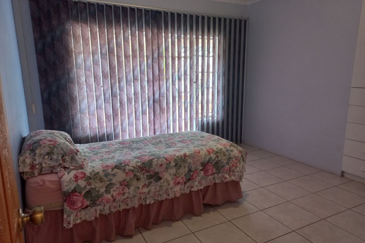 A bedroom featuring tiled flooring, built-in cupboards, and vertical blinds covering the window.