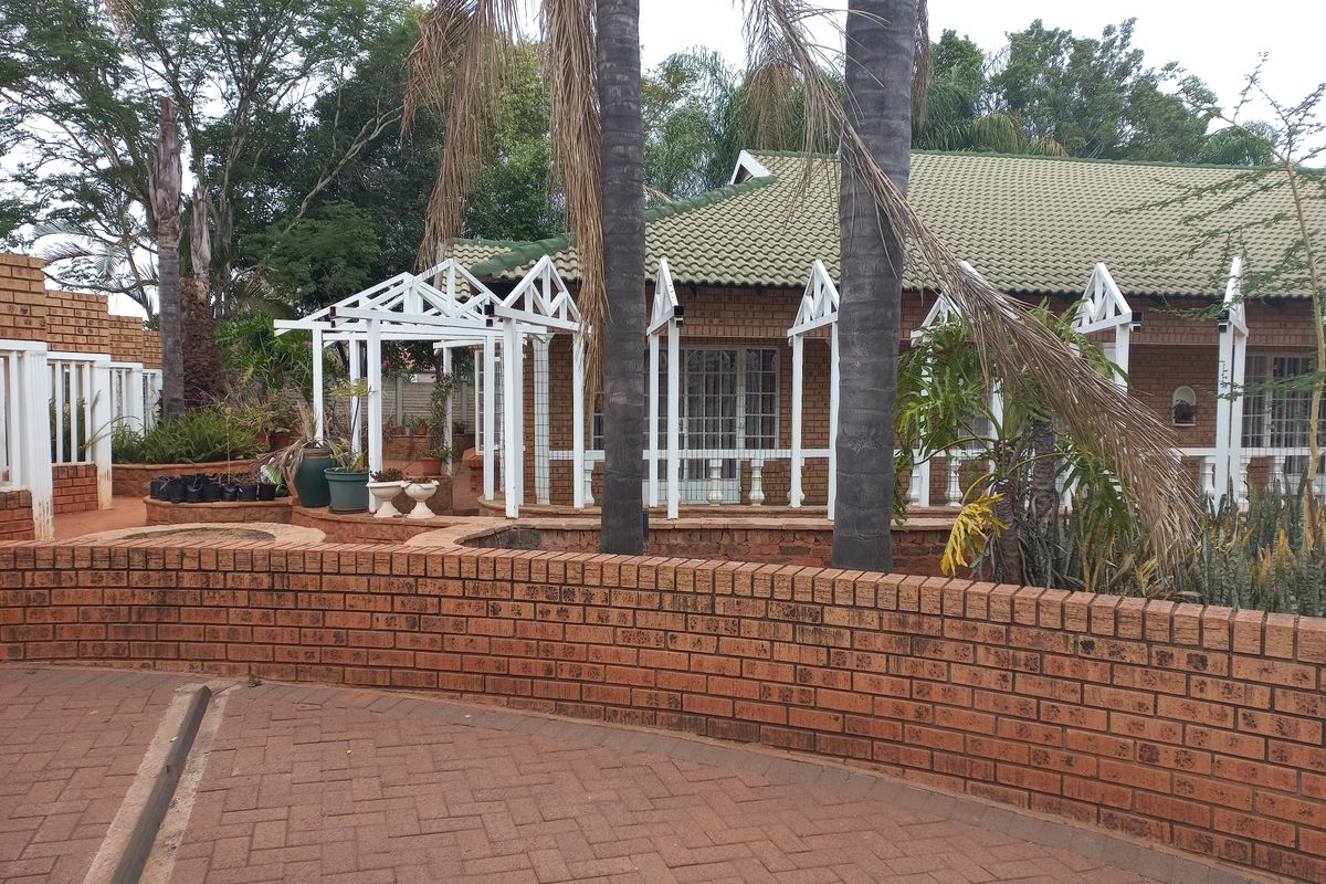 Rear exterior view featuring a brick paved area, a low brick retaining wall, and a white timber pergola structure attached to the house.
