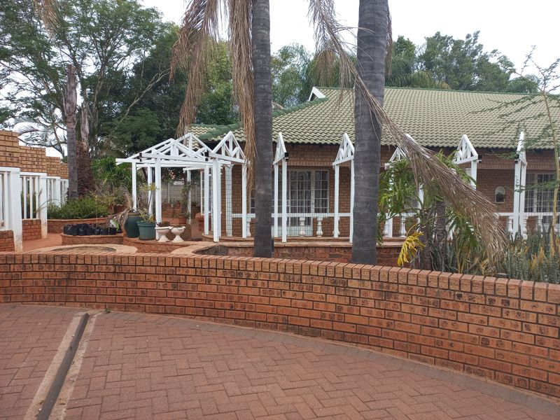 Rear exterior view featuring a brick paved area, a low brick retaining wall, and a white timber pergola structure attached to the house.
