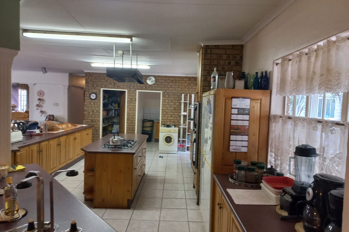 Spacious kitchen featuring wooden cabinetry, a central island with a gas hob, tiled flooring, and a distinct brick feature wall with an adjoining pantry.