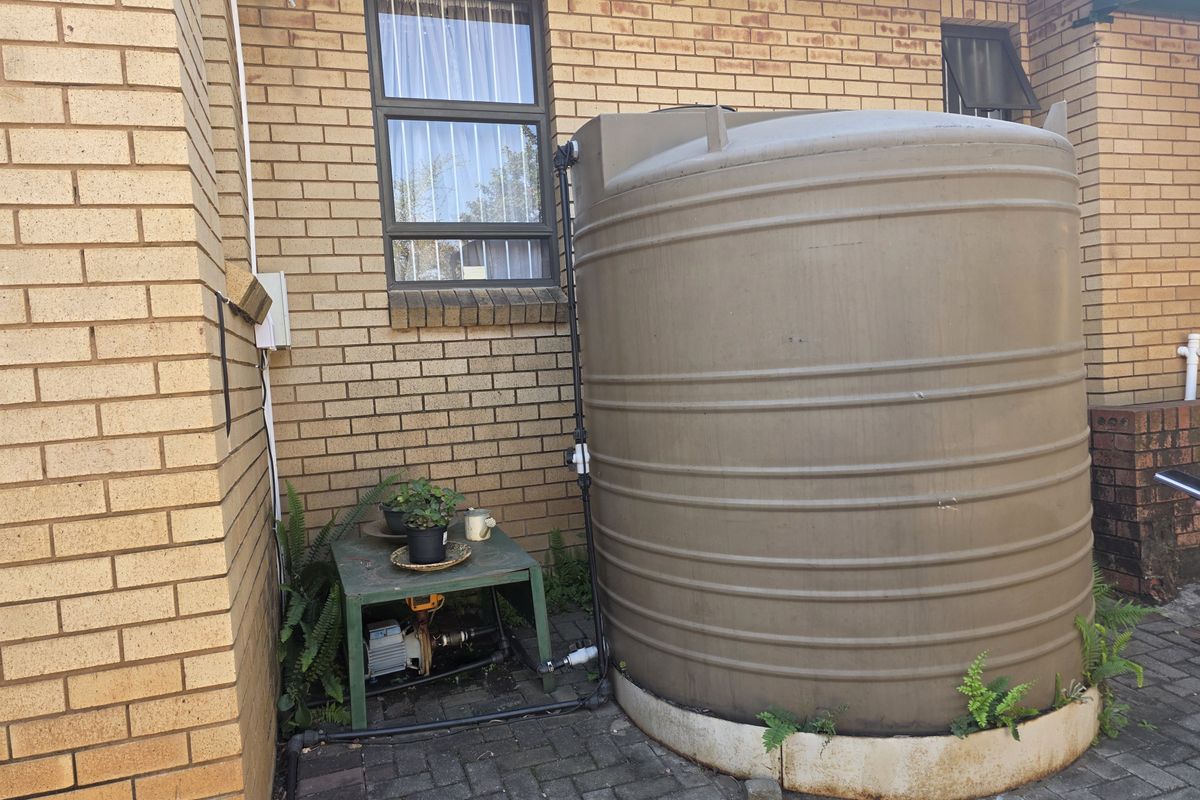 Exterior rear area featuring a large water storage tank and pump system installed against a face brick wall with paved ground.