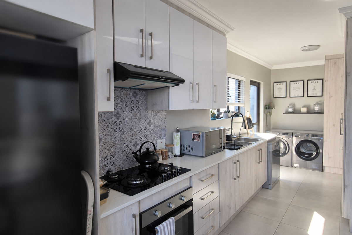 Modern kitchen featuring light wood-look cabinetry, a patterned tile backsplash, gas hob, built-in oven, and an integrated laundry area with tiled flooring.