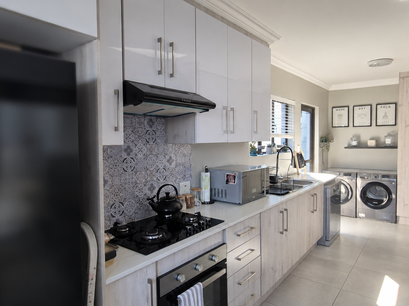 Modern kitchen featuring light wood-look cabinetry, a patterned tile backsplash, gas hob, built-in oven, and an integrated laundry area with tiled flooring.