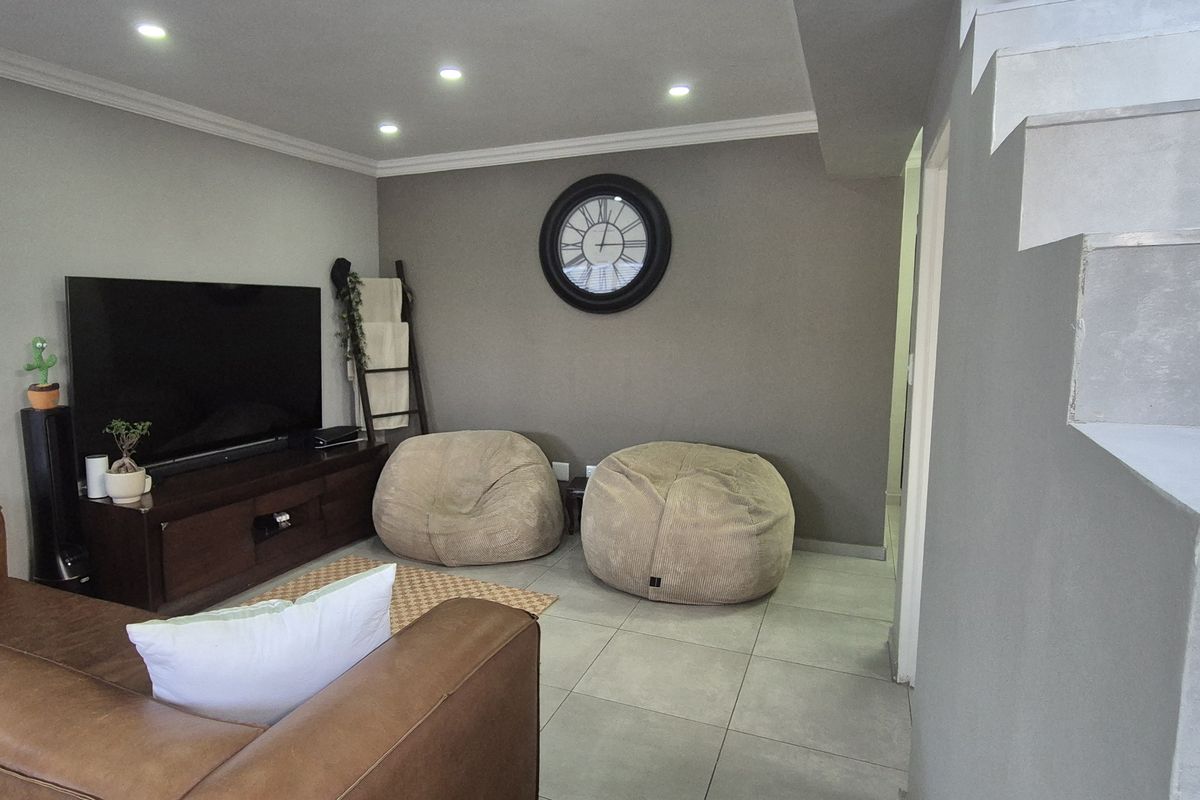 A modern living room featuring tiled flooring, recessed downlighting, and a staircase with a metal railing, creating a clean and contemporary open-plan feel.