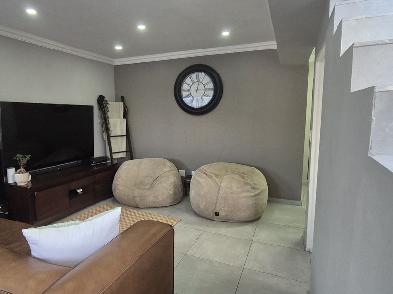 A modern living room featuring tiled flooring, recessed downlighting, and a staircase with a metal railing, creating a clean and contemporary open-plan feel.