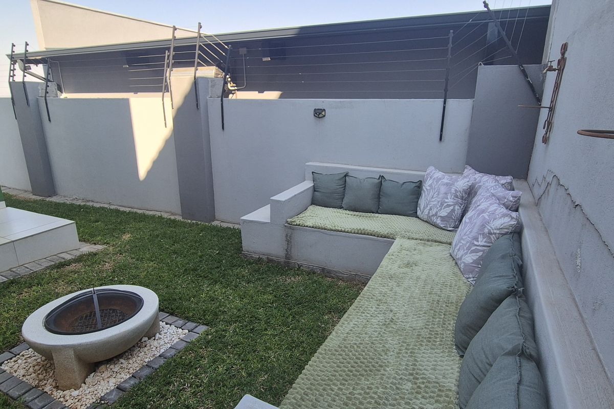 A private rear courtyard featuring a built-in concrete seating area, a fire pit, and a small lawn enclosed by a boundary wall with electric fencing.