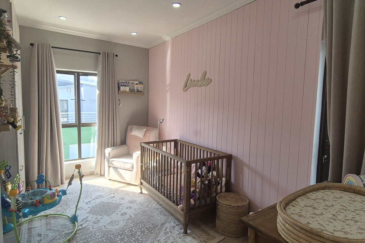 A well-maintained bedroom featuring a soft pink vertical paneling accent wall, recessed downlighting, and neutral timber-look flooring.