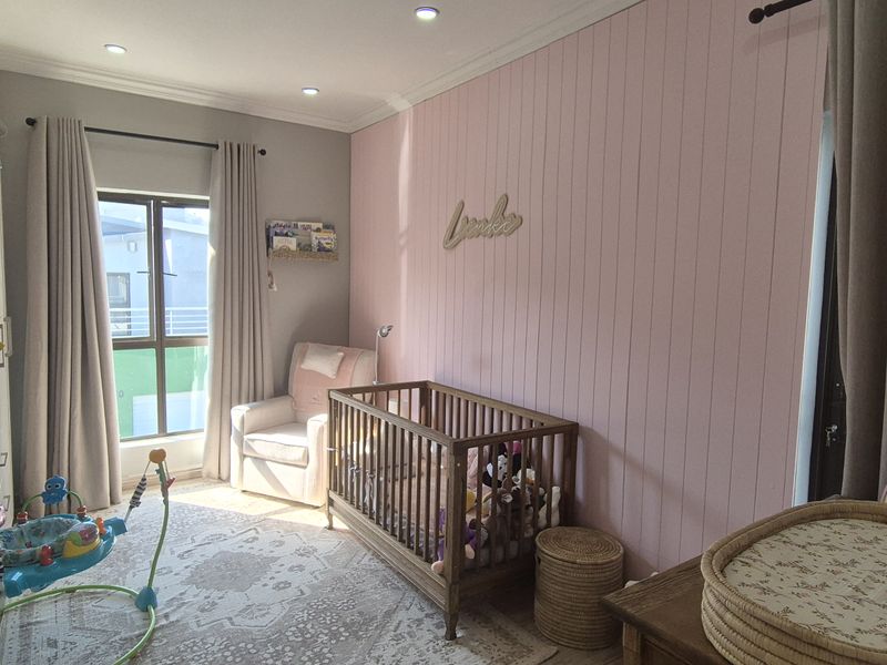 A well-maintained bedroom featuring a soft pink vertical paneling accent wall, recessed downlighting, and neutral timber-look flooring.