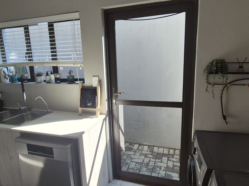 Modern kitchen area featuring light wood-grain cabinetry, stainless steel sink, integrated dishwasher, and direct access to an external paved courtyard.