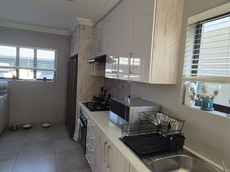Modern kitchen featuring light wood-look cabinetry, stone-effect countertops, gas hob, extractor fan, and tiled flooring with ample natural light.