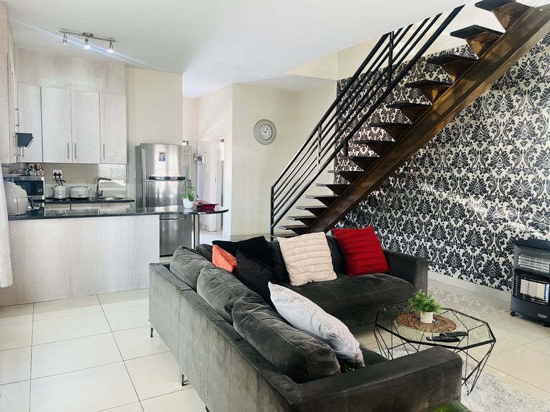 Open-plan living area featuring a modern kitchen with granite countertops and a striking staircase with metal railings and decorative wallpaper.