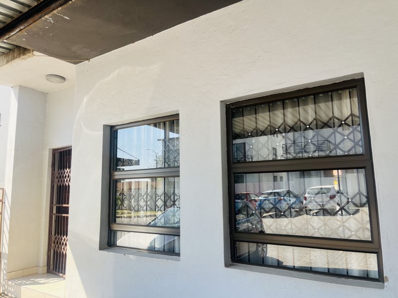 Front facade of the townhouse featuring white rendered walls, dark aluminium window frames with integrated security bars, and a secure entrance gate.
