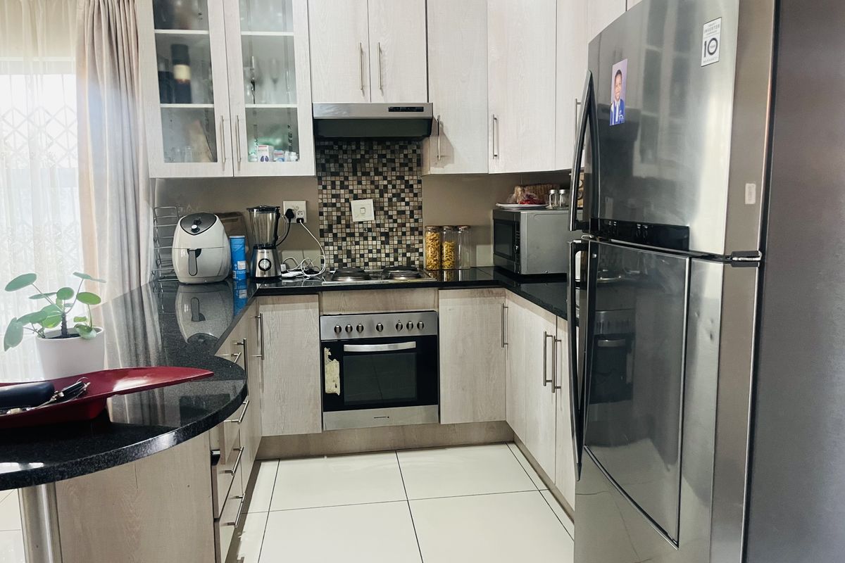 A functional kitchen featuring light wood-finish cabinetry, black granite countertops, built-in oven and hob, and tiled flooring.
