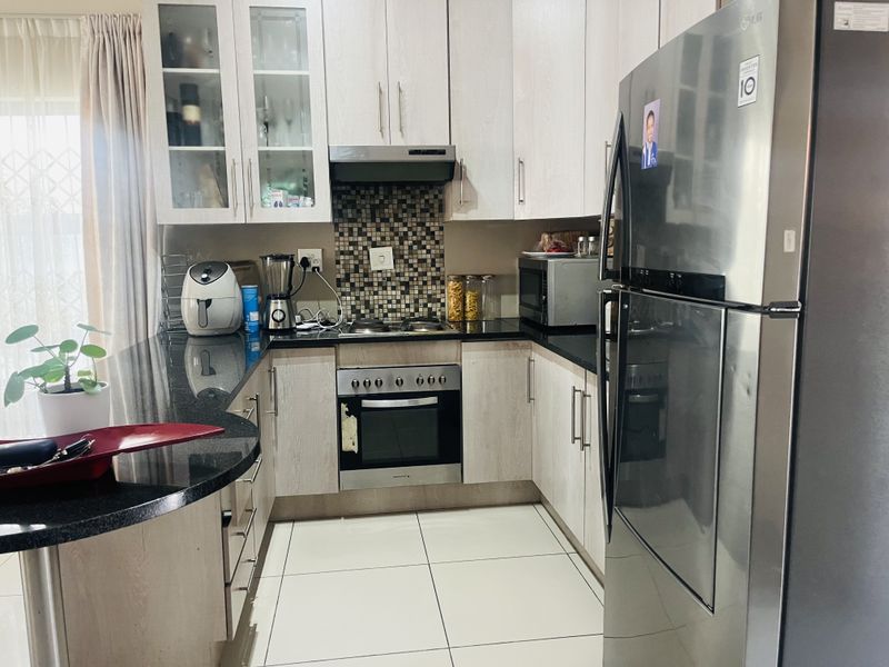 A functional kitchen featuring light wood-finish cabinetry, black granite countertops, built-in oven and hob, and tiled flooring.