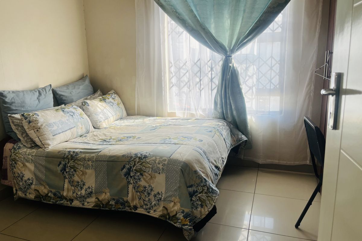 A compact bedroom featuring tiled flooring and a window fitted with a security gate, providing natural light.