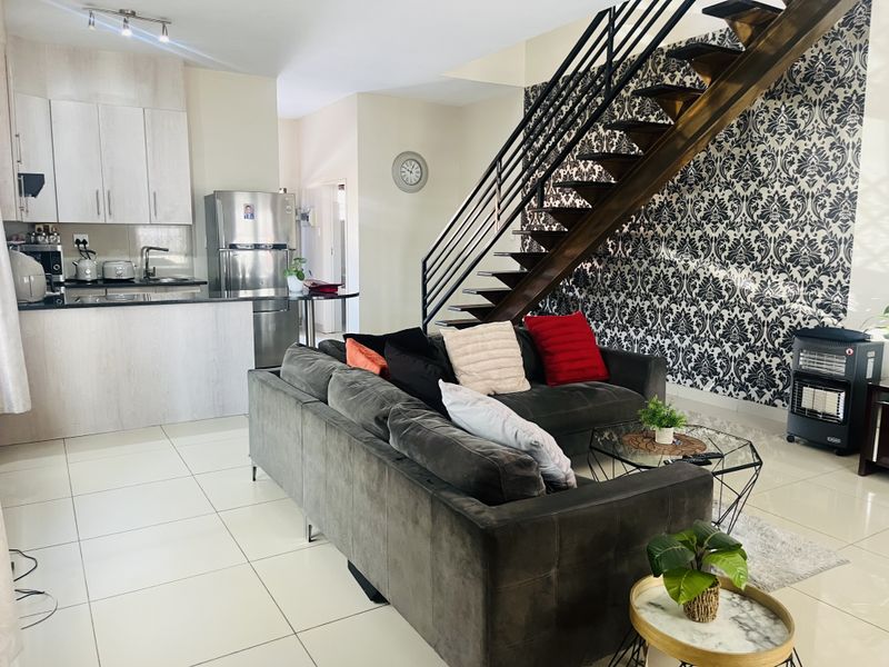 Open-plan living area featuring a modern kitchen with granite countertops and a striking staircase with metal railings and decorative wallpaper.