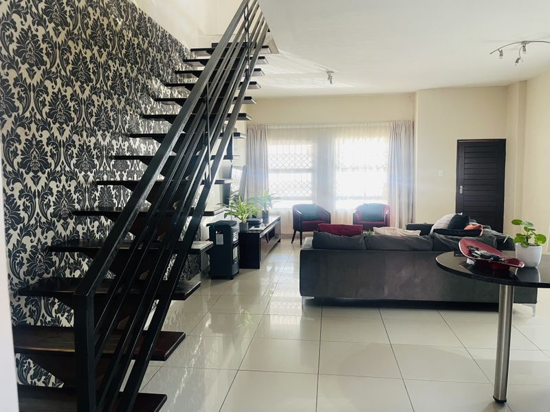 Spacious open-plan living area featuring a modern open-tread staircase, large windows with security bars, and polished porcelain floor tiles.