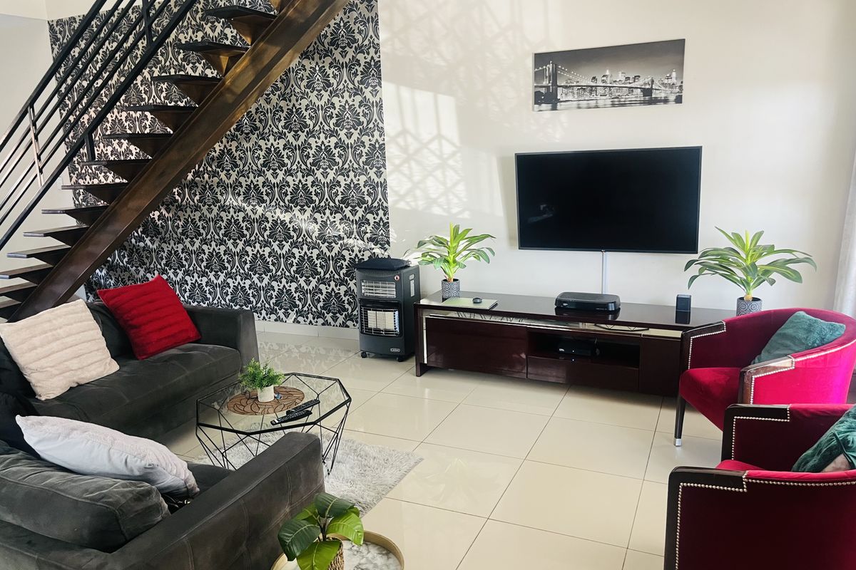 Spacious living room featuring a modern open-tread staircase with metal balustrade, tiled flooring, and a striking feature wallpaper wall.