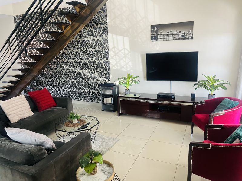 Spacious living room featuring a modern open-tread staircase with metal balustrade, tiled flooring, and a striking feature wallpaper wall.