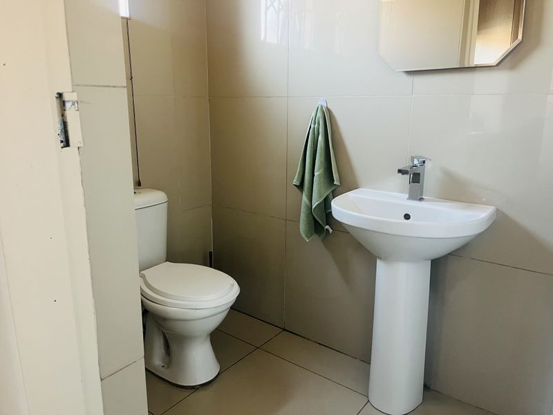 A functional bathroom featuring a pedestal basin, toilet, and neutral wall and floor tiling.