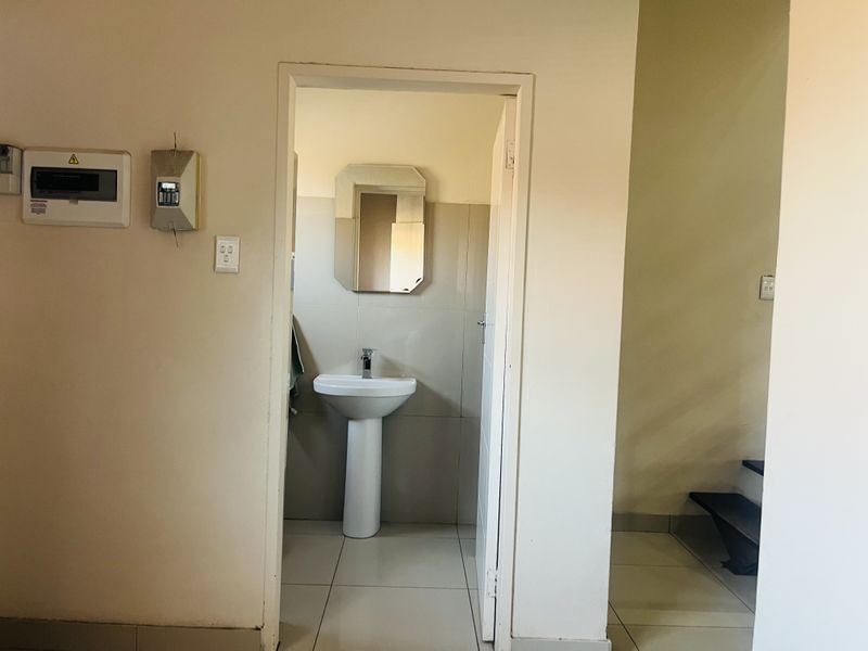 A functional guest bathroom featuring a pedestal basin and tiled finishes, located adjacent to the main living area and staircase.