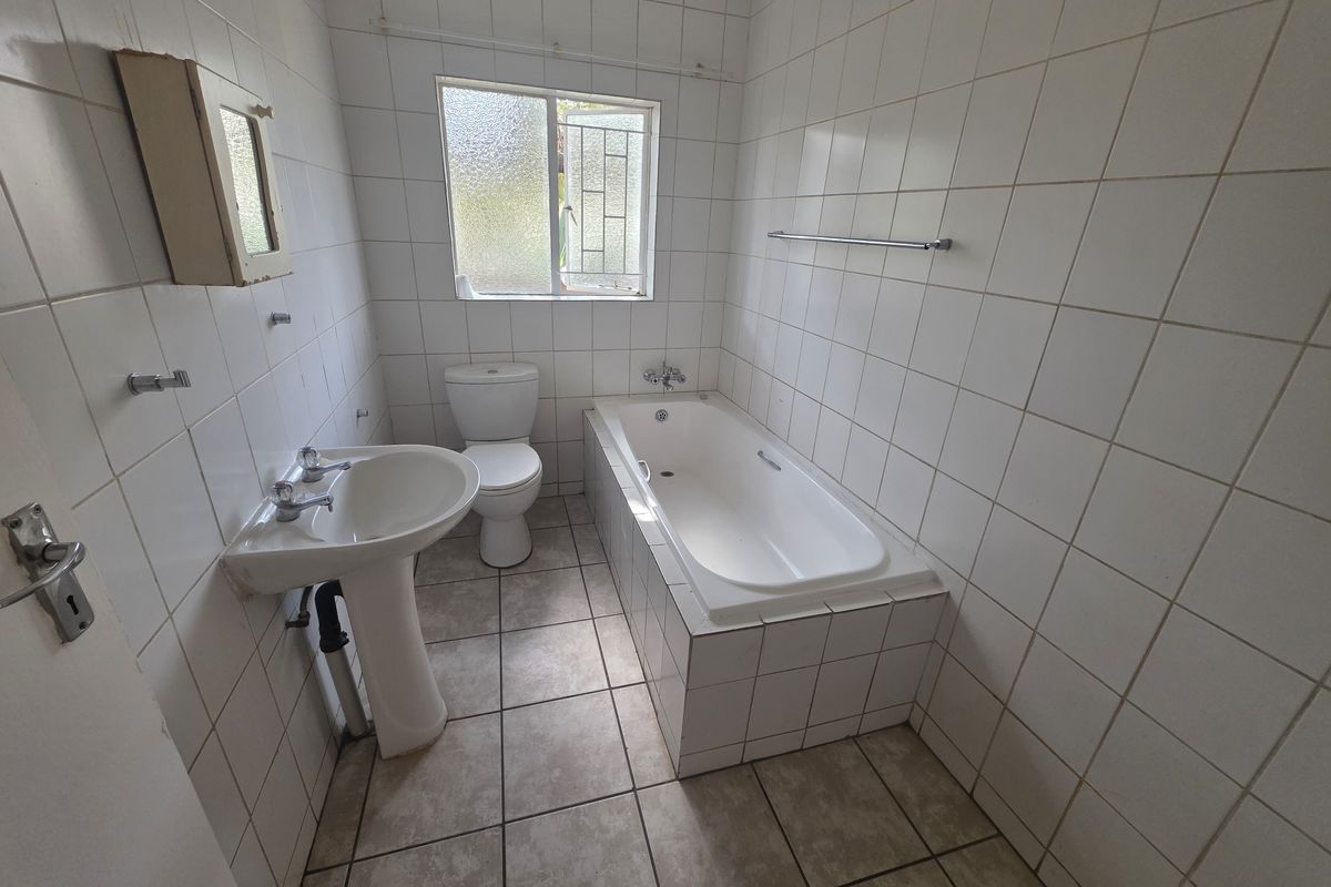 A functional bathroom featuring a pedestal basin, built-in bathtub, and toilet with full-height wall tiling and tiled flooring.