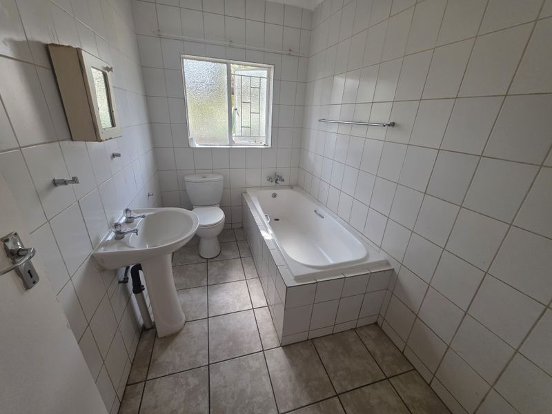 A functional bathroom featuring a pedestal basin, built-in bathtub, and toilet with full-height wall tiling and tiled flooring.