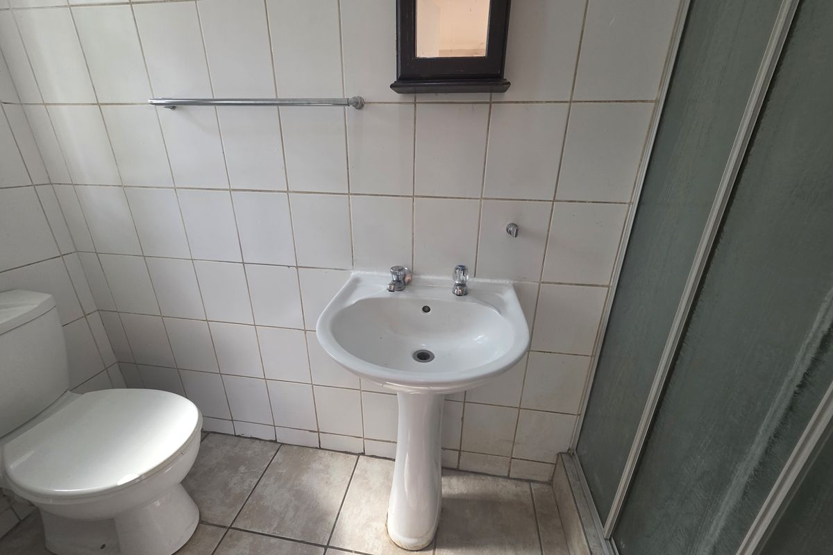 A functional bathroom featuring a pedestal basin, toilet, and shower enclosure with tiled walls and flooring, currently in need of cosmetic updates.