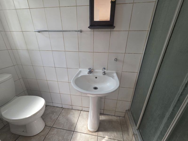 A functional bathroom featuring a pedestal basin, toilet, and shower enclosure with tiled walls and flooring, currently in need of cosmetic updates.