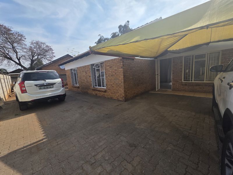 Front exterior view of a face brick house featuring a paved driveway and a shade cloth carport structure.