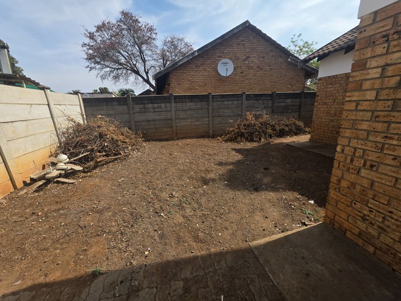 A rear exterior view of the property featuring a paved patio area and a large, unlandscaped garden space enclosed by precast concrete boundary walls.