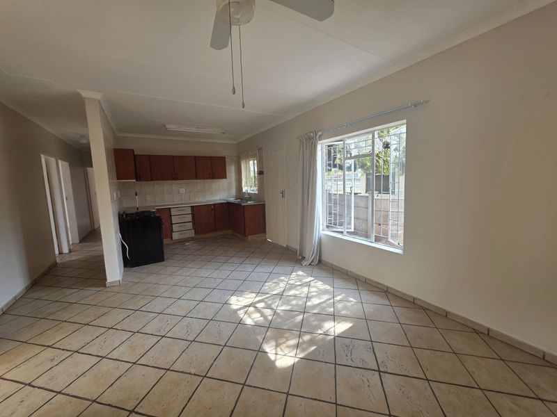 An open-plan living and kitchen area featuring tiled flooring, built-in wooden cabinetry, and large windows with security bars.