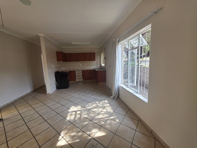 Open plan living and kitchen area featuring tiled flooring, built-in cabinetry, and large windows with security bars.