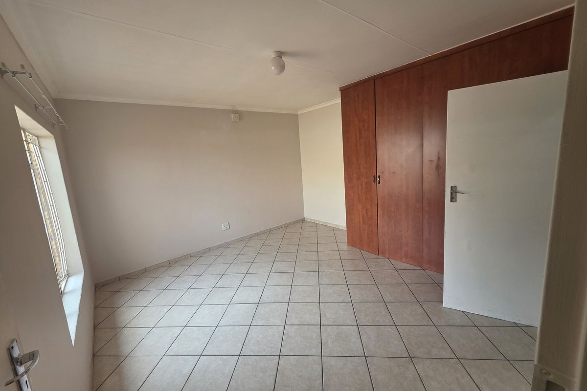 A clean, empty bedroom featuring neutral tiled flooring and built-in wooden cupboards, offering a versatile space ready for personalization.