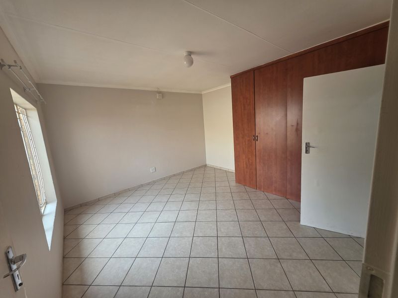 A clean, empty bedroom featuring neutral tiled flooring and built-in wooden cupboards, offering a versatile space ready for personalization.