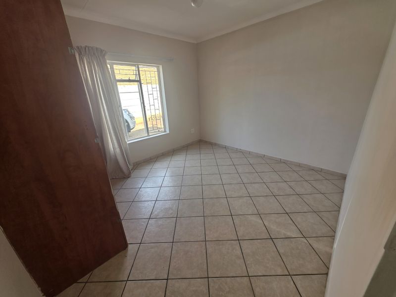 A clean, empty bedroom featuring neutral tiled flooring and a window fitted with security bars, offering a blank canvas for personalization.