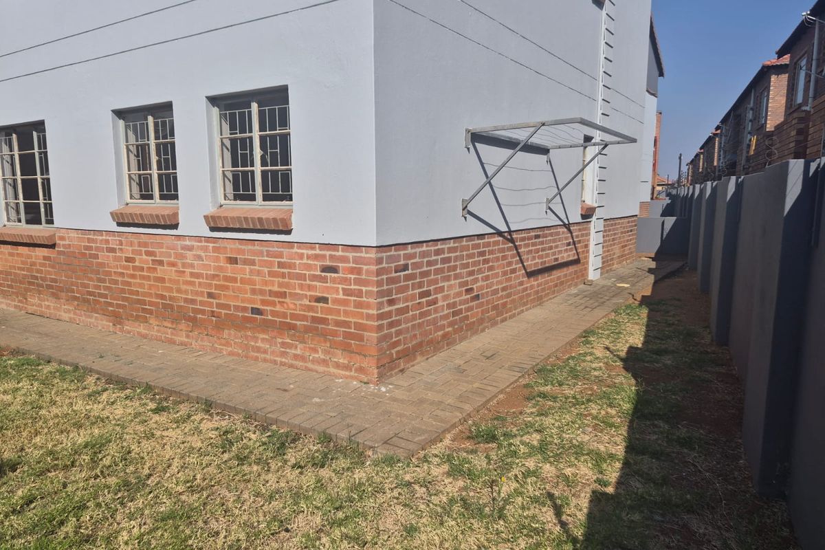Rear exterior view of the apartment building featuring a brick and plastered facade, steel window frames, and paved walkway area.
