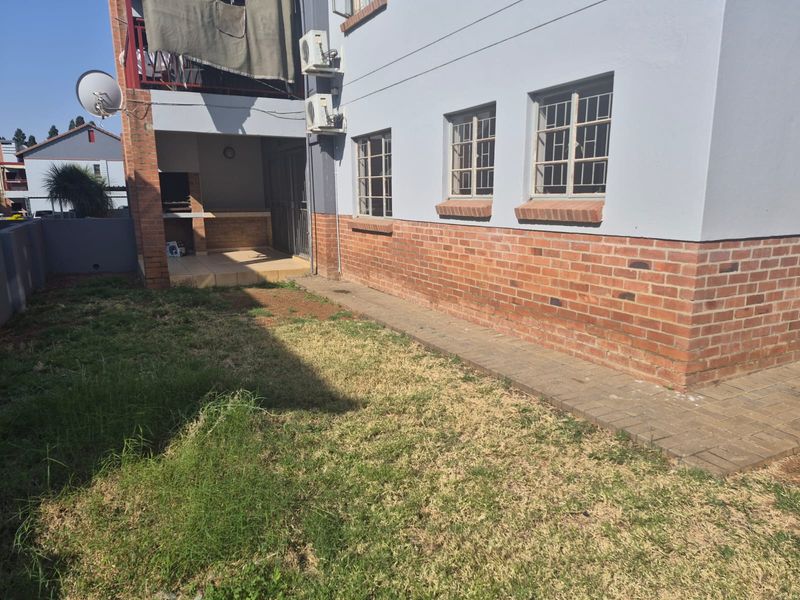 Rear exterior view of the apartment featuring a brick facade, security-barred windows, a paved walkway, and a built-in braai area.